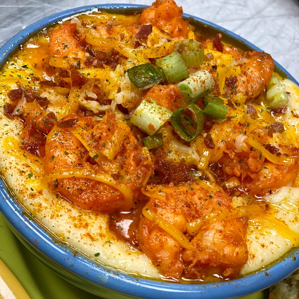 Shrimp and grits with cheese, bacon, and green onions in a blue bowl, a soul-food dish.