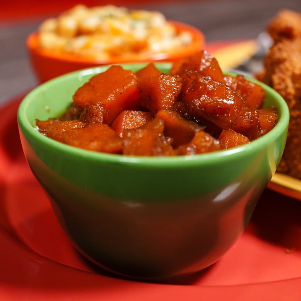 A vibrant green bowl filled with glistening candied yams, with macaroni and cheese in the background.