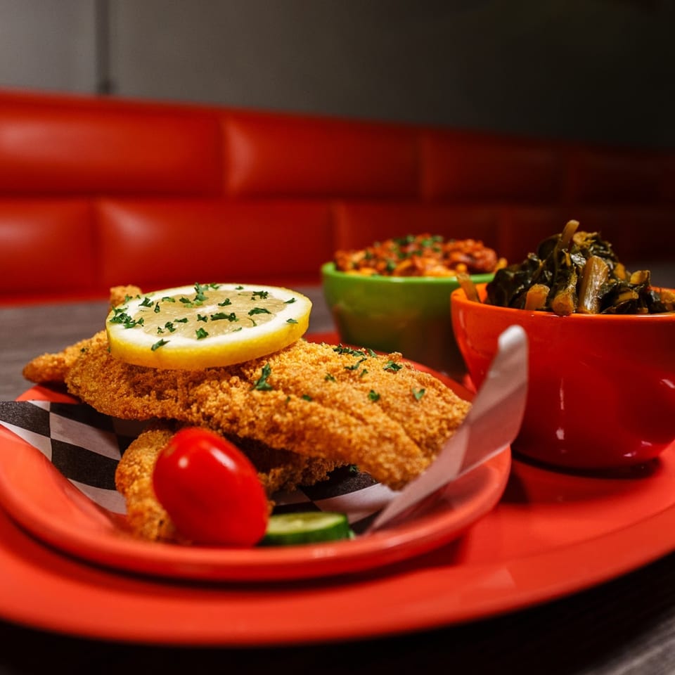 Fried fish with a lemon slice, collard greens, and macaroni and cheese on a red tray.