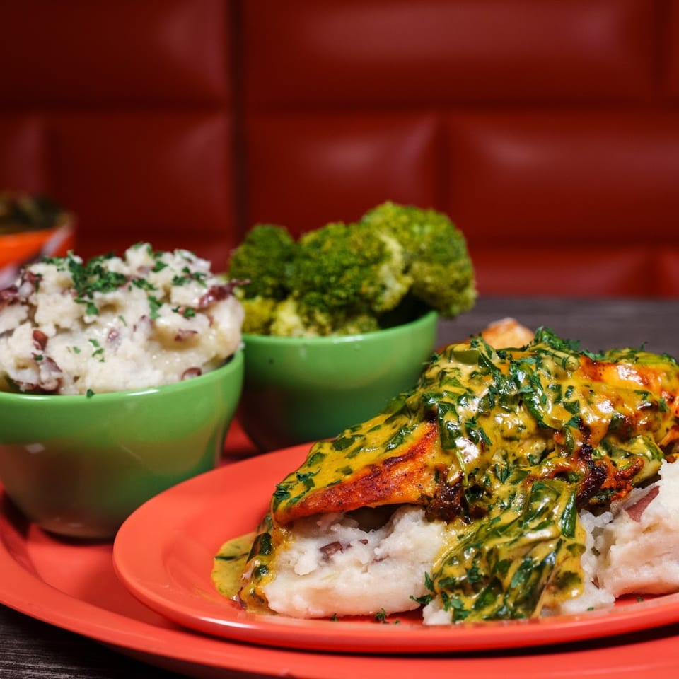 Soul food meal with chicken and gravy over mashed potatoes, with sides of mashed potatoes and broccoli.