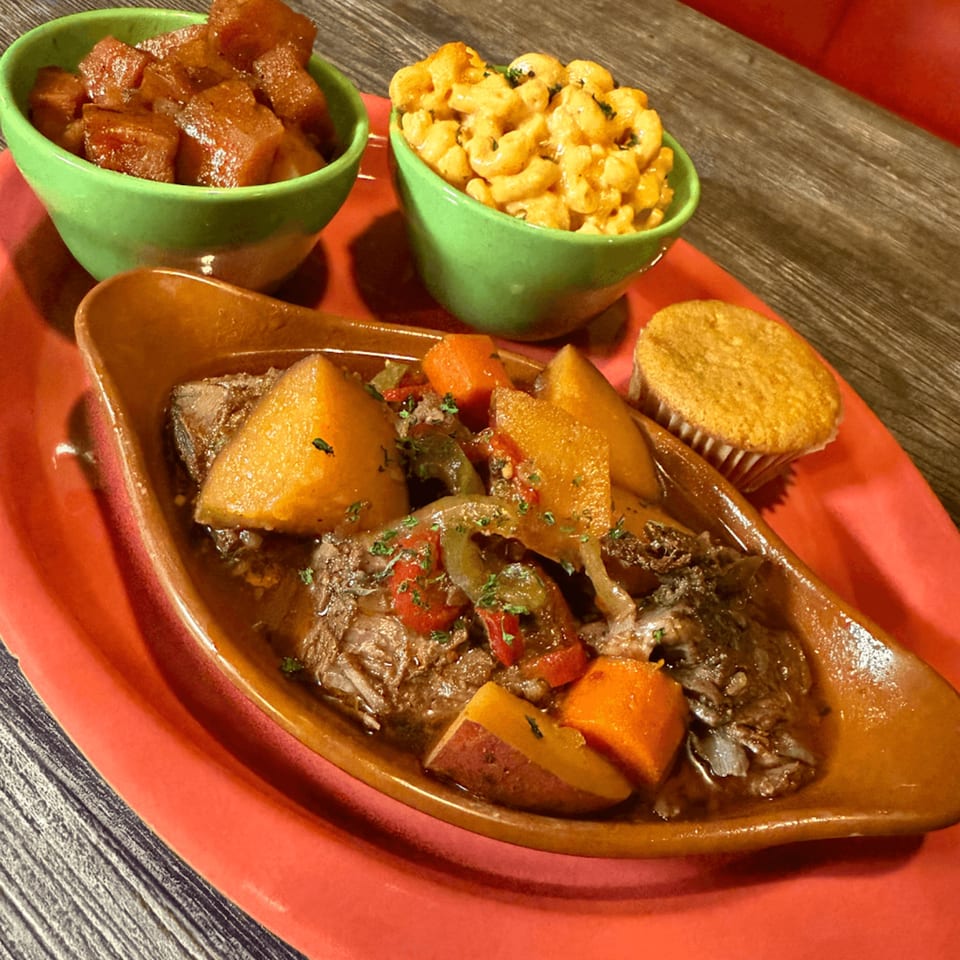 A hearty meal with beef stew, macaroni and cheese, candied yams, and a cornbread muffin.