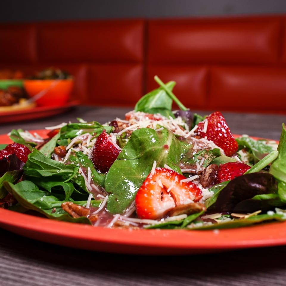 Strawberry and spinach salad with pecans and shredded cheese on a red plate at The Neighborhood Gem.