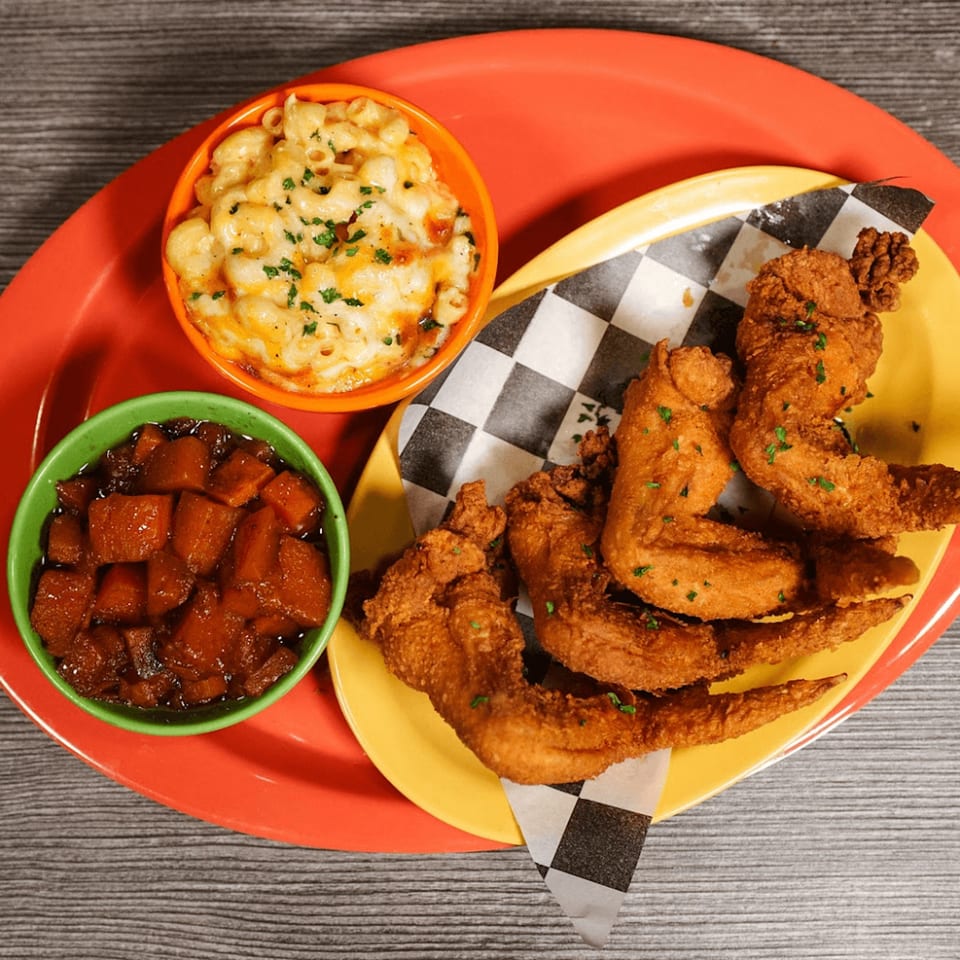 Fried chicken wings, mac and cheese, and candied yams on a red and yellow plate.