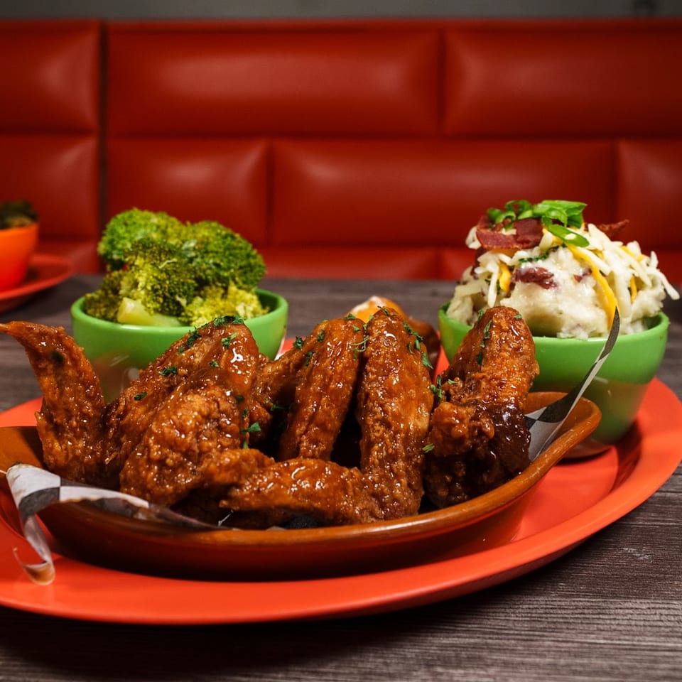 Soul food meal with glazed chicken wings, mashed potatoes, and broccoli on a red plate.